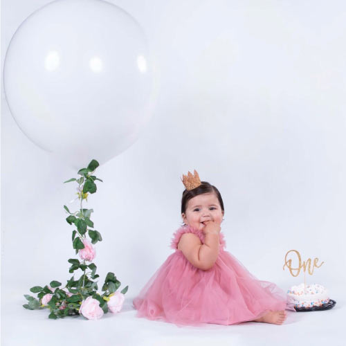 Baby girl in a pink tulle dress celebrating her first birthday with a giant white balloon and smash cake