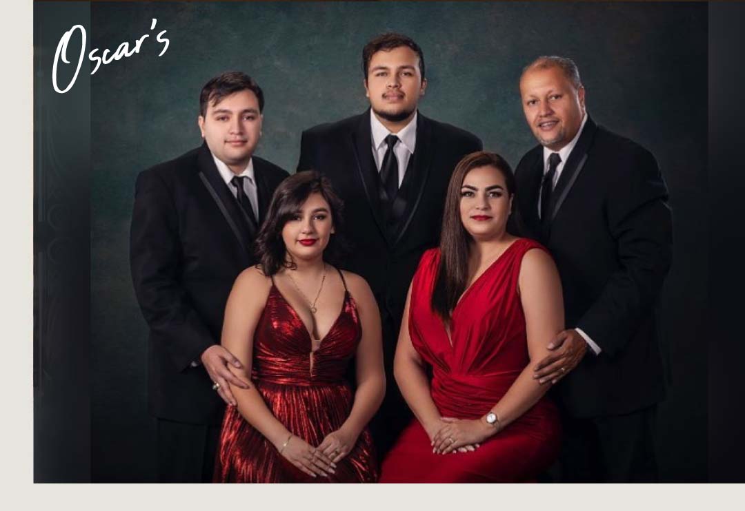 Family of five in formal black suits and red dresses, elegant studio portrait on dark green backdrop