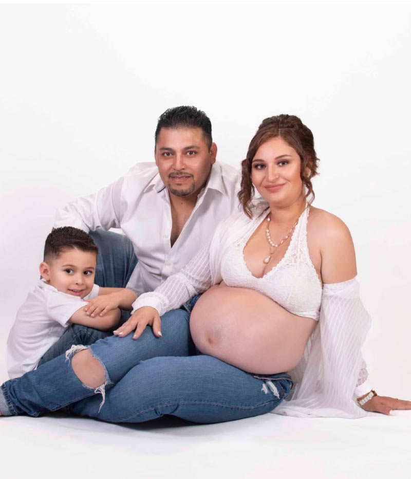 Family portrait of expecting parents and their young son, maternity photoshoot on white studio backdrop