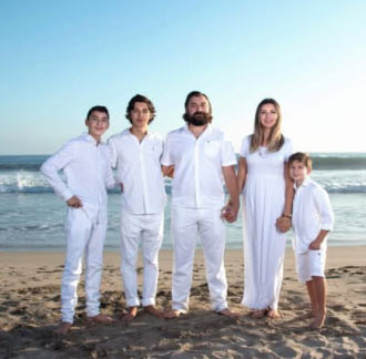 Family of five in white outfits posing together on the beach at sunset