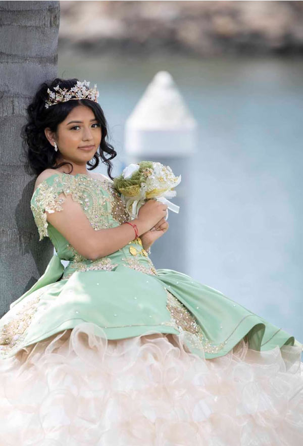 Quinceañera in a sage green and gold ball gown with tiara, outdoor portrait session