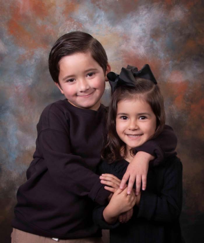 Young brother and sister embracing, studio portrait on painted backdrop