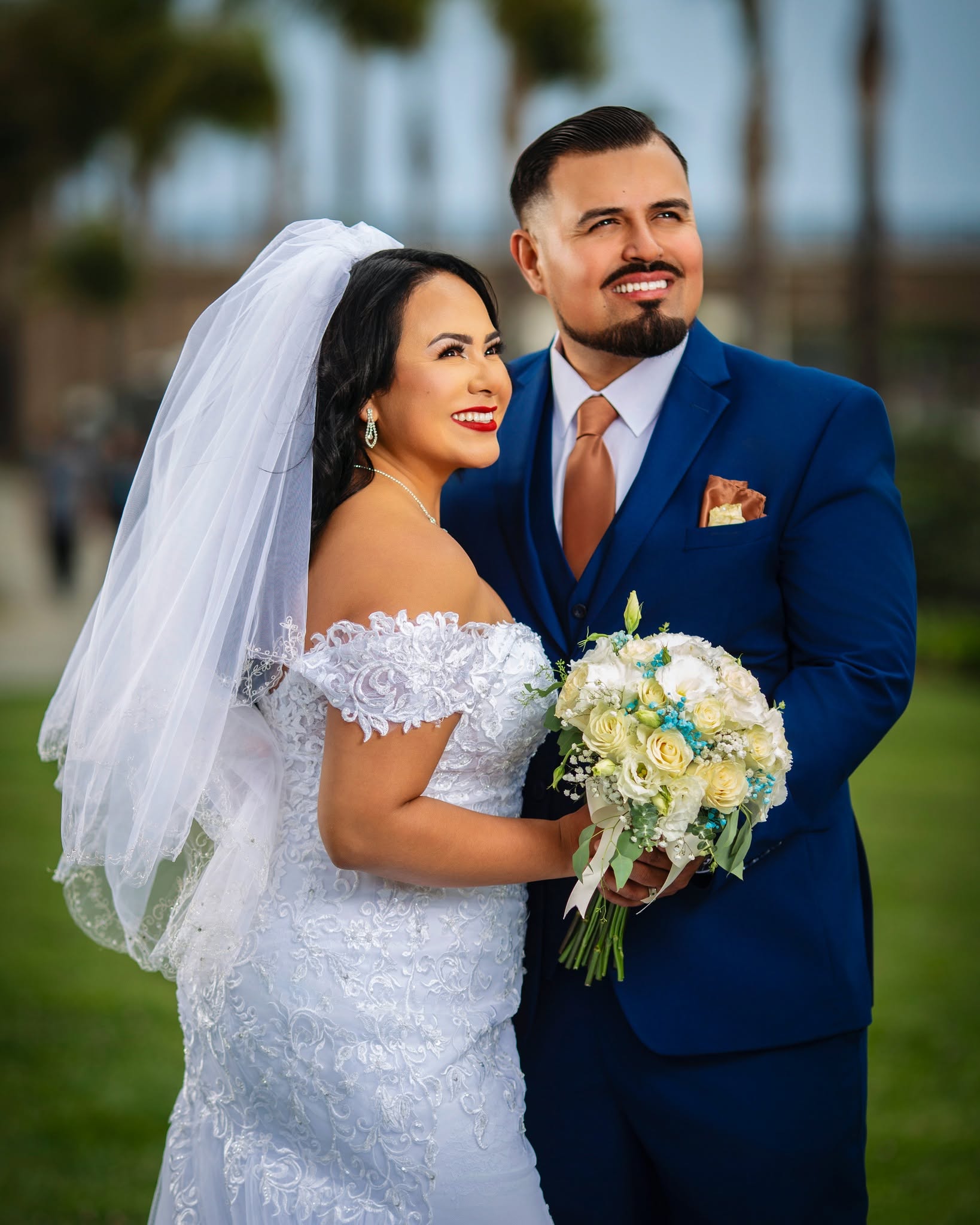Bride and groom smiling together outdoors, bride in lace off-shoulder gown holding white bouquet, wedding photography in Ventura County