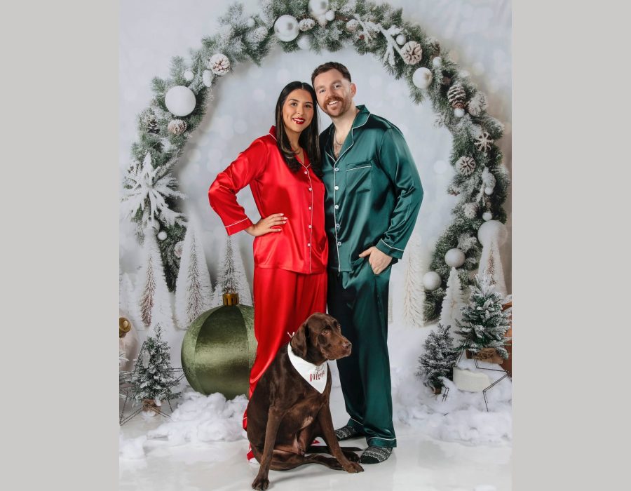Couple in matching silk pajamas with their dog posing for a holiday-themed Christmas photoshoot