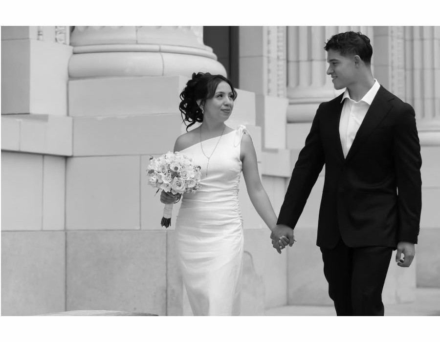Black and white wedding photo of bride and groom holding hands walking past classical columns