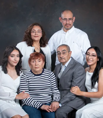 Three-generation family portrait of grandparents seated at center, their adult children standing behind, and two granddaughters in white dresses on either side.