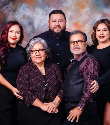 Family portrait of parents in burgundy and black outfits seated in front, with their adult son and two daughters dressed in black standing behind against a painted backdrop.