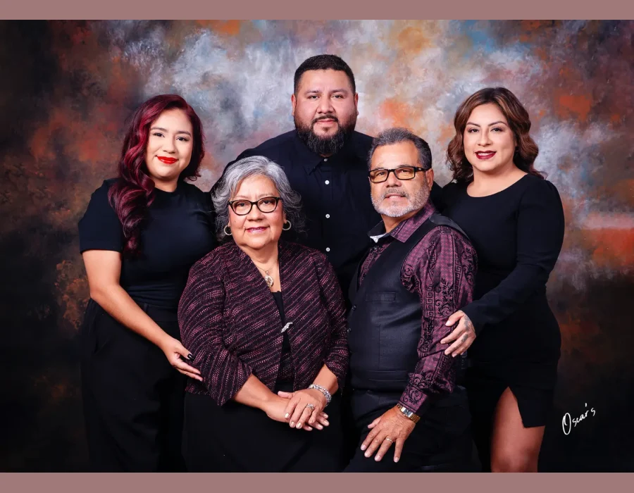 Family portrait of parents in burgundy and black outfits seated in front, with their adult son and two daughters dressed in black standing behind against a painted backdrop.