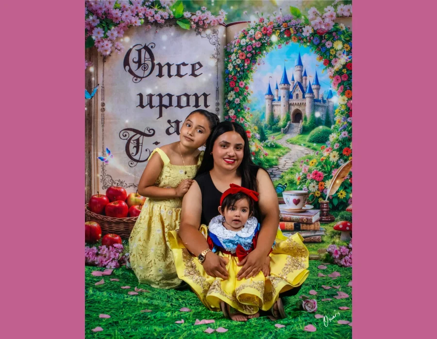Mother with her two daughters on a storybook-themed set with a castle and "Once Upon a Time" book backdrop, the baby in a yellow princess dress and the older girl in yellow lace.