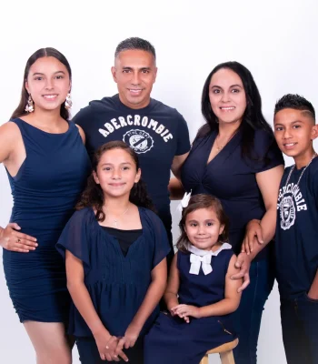 Family of six in coordinated navy outfits, including parents, a teen daughter, a son, and two young daughters, posed against a bright white studio backdrop.