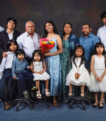 Extended family portrait of twelve, including a grandfather, parents, and children of all ages, gathered around a smiling young woman holding a colorful bouquet.