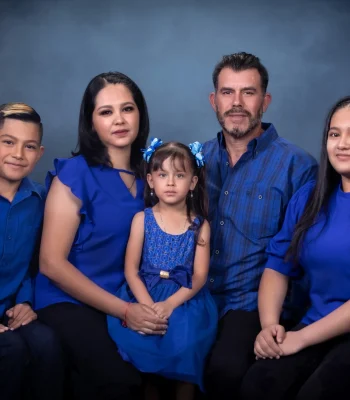 Family of five in coordinated royal blue outfits, with the youngest daughter seated at center, posed against a dark blue studio backdrop.