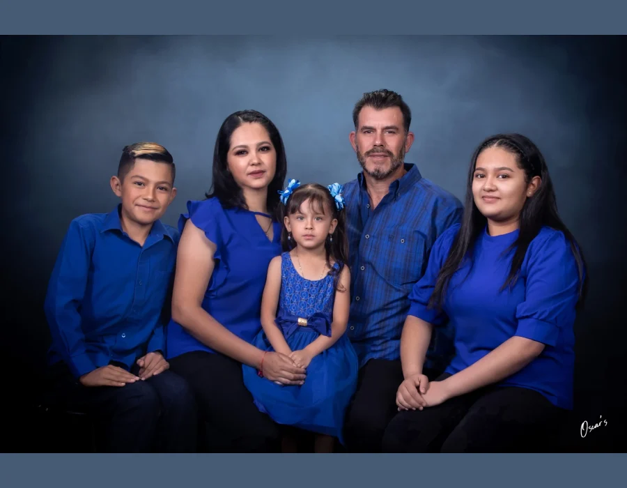 Family of five in coordinated royal blue outfits, with the youngest daughter seated at center, posed against a dark blue studio backdrop.