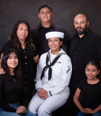 Family portrait celebrating a daughter in a U.S. Navy white dress uniform, seated at center and surrounded by her parents and three siblings dressed in black.