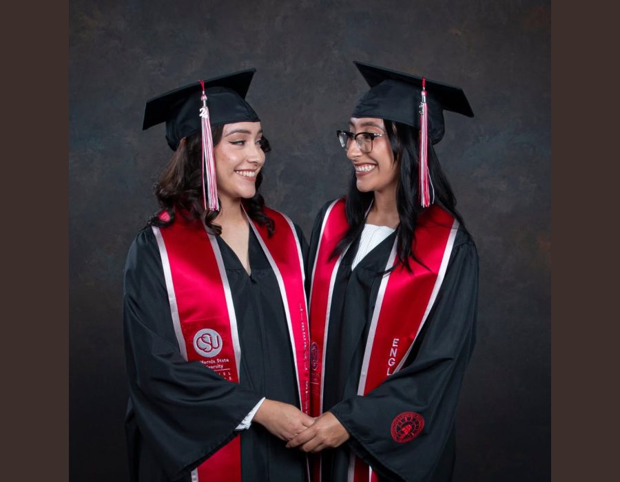 Two college graduates in cap and gown with red honor stoles holding hands, studio graduation portrait