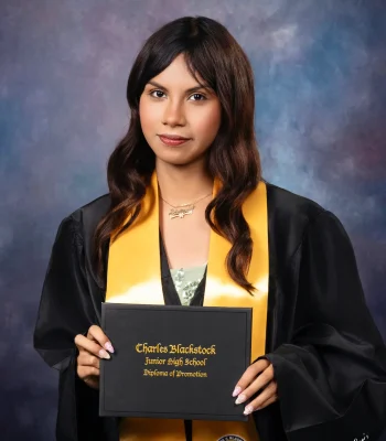 Student with wavy brown hair in a black gown and gold stole, holding a Charles Blackstock Junior High School diploma of promotion.