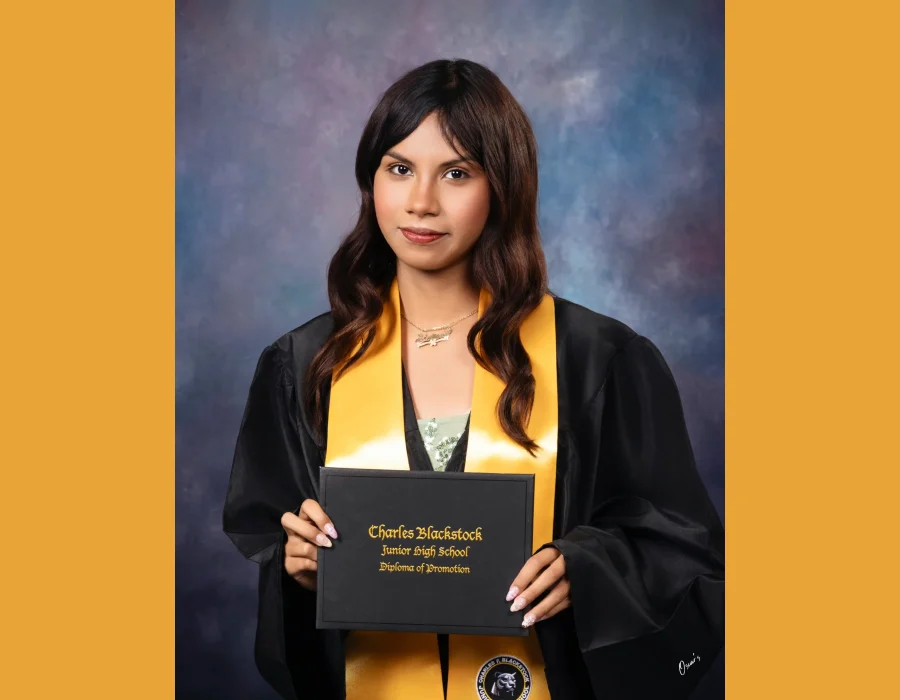 Student with wavy brown hair in a black gown and gold stole, holding a Charles Blackstock Junior High School diploma of promotion.