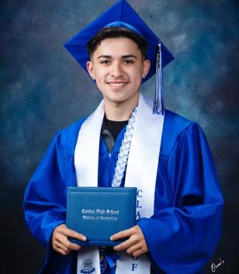Smiling graduate in a royal blue cap and gown with a white Class of 2026 stole and braided lei, holding a Condor High School diploma.