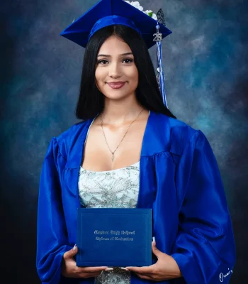 Graduate with long black hair in a blue gown and a flower-decorated cap with a "26" tassel charm, holding a Condor High School diploma.