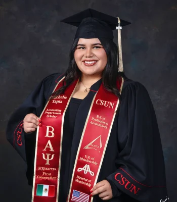University graduate in a black CSUN gown and a red embroidered stole reading "Accounting Department Scholar," "First Generation," and "B.S. of Professional Accountancy," with Mexican and American flag patches.