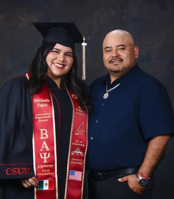 Smiling CSUN accounting graduate in her cap, gown and embroidered red stole, posing beside her father in a navy button-up shirt.