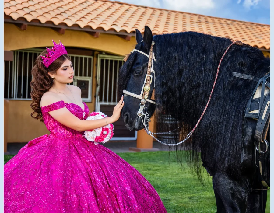 Quinceañera portrait in a fuchsia sequined gown, gently touching a black horse outside a stable