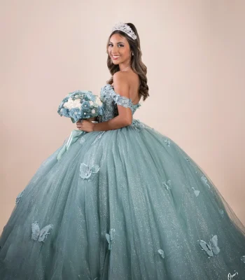 Quinceañera portrait in a sage green beaded gown, smiling over her shoulder against a soft pink studio backdrop