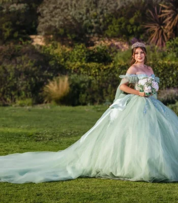 Quinceañera portrait in a mint green tulle gown with a long train, standing in a garden at golden hour