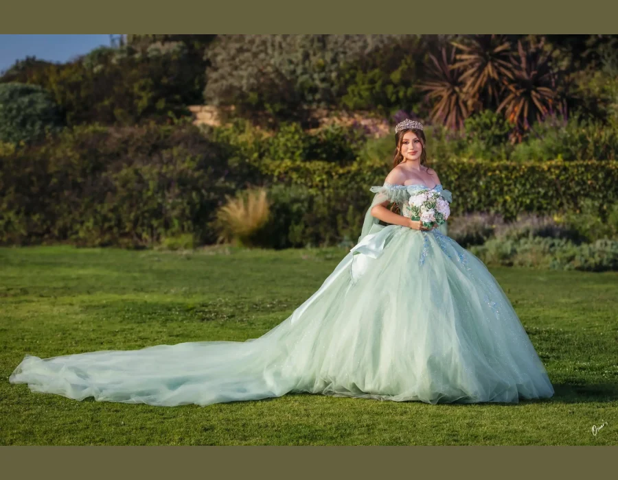 Quinceañera portrait in a mint green tulle gown with a long train, standing in a garden at golden hour