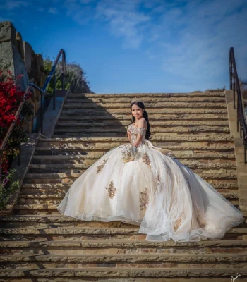 Quinceañera portrait in a champagne beaded ball gown, descending outdoor stone steps with ocean bluffs behind her