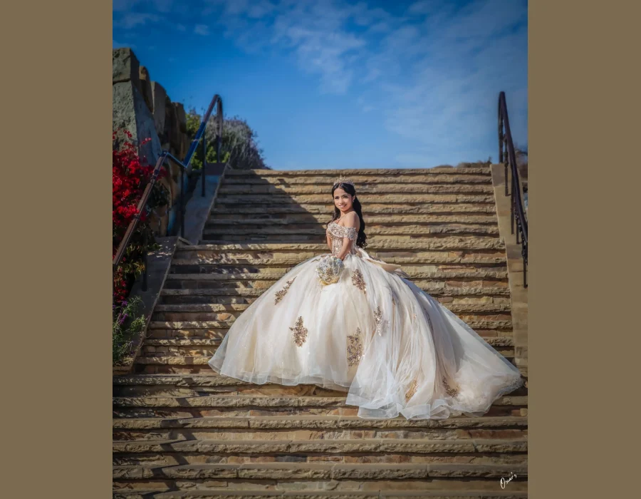 Quinceañera portrait in a champagne beaded ball gown, descending outdoor stone steps with ocean bluffs behind her