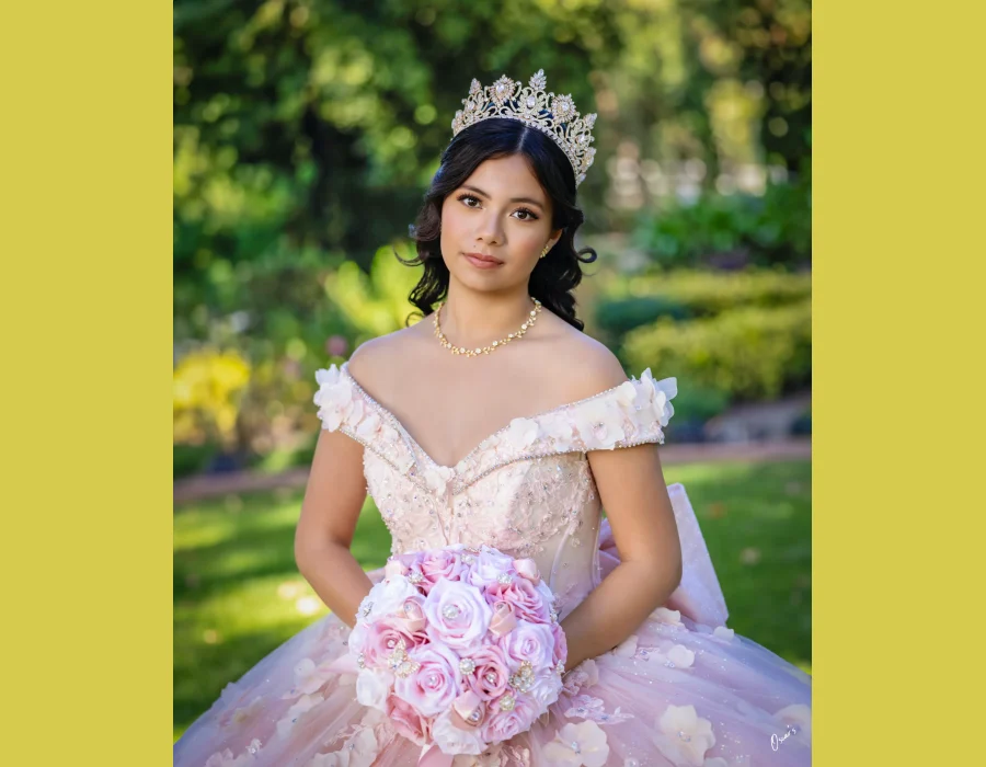 Quinceañera close-up portrait in a blush off-the-shoulder gown with floral trim and a gold tiara, holding a pink rose bouquet
