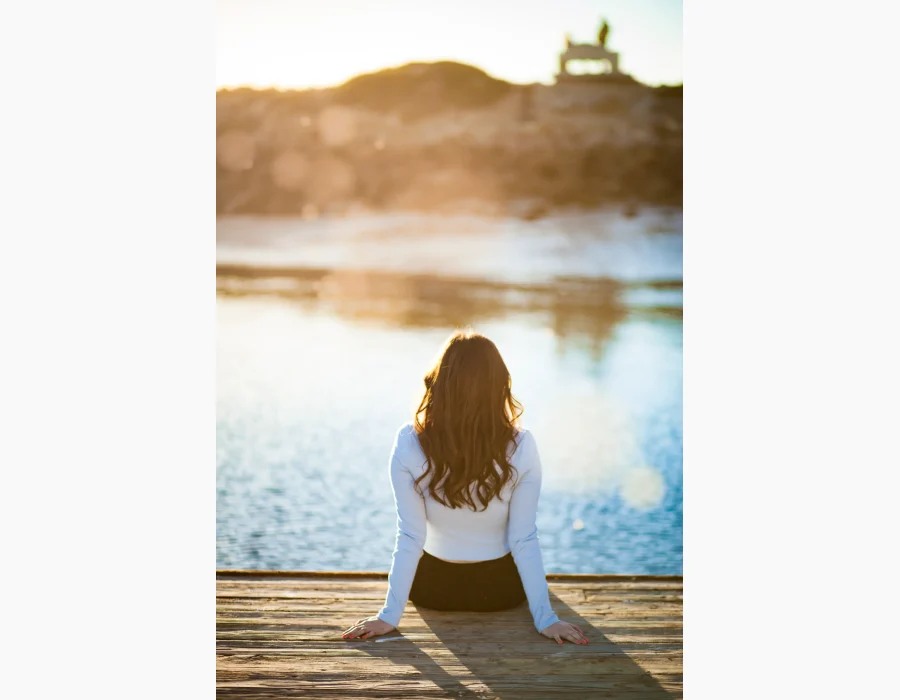Quinceañera portrait from behind, seated on a dock at sunset overlooking the water