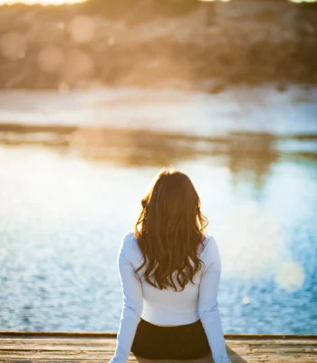 Quinceañera portrait from behind, seated on a dock at sunset overlooking the water