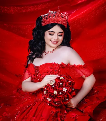 Quinceañera close-up portrait in a red sequined gown with a matching red crystal tiara and necklace, holding a red rose bouquet against a red backdrop