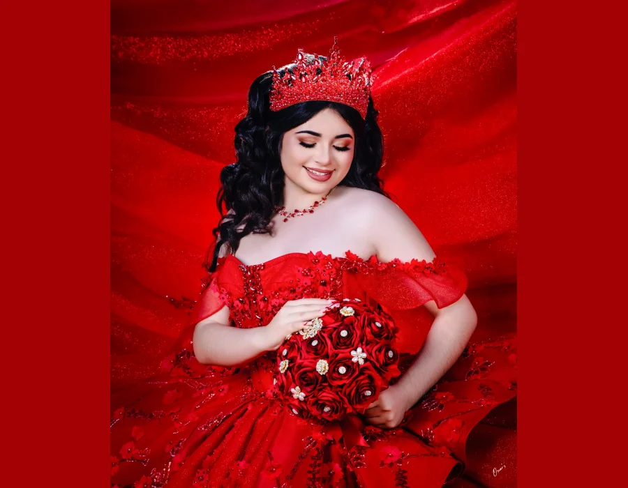Quinceañera close-up portrait in a red sequined gown with a matching red crystal tiara and necklace, holding a red rose bouquet against a red backdrop