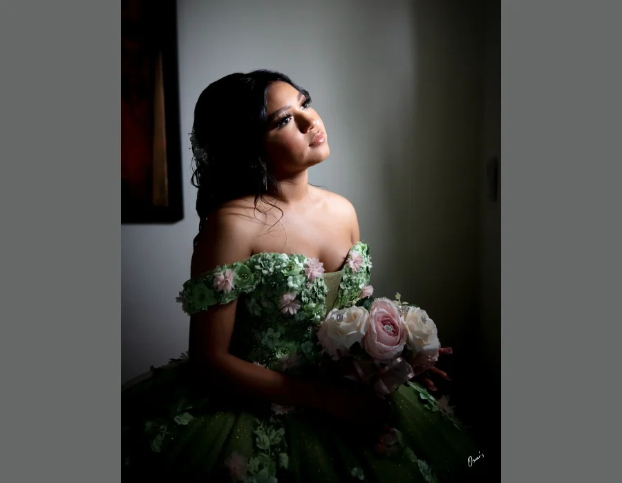 Quinceañera close-up portrait in a red sequined gown with a matching red crystal tiara and necklace, holding a red rose bouquet against a red backdrop