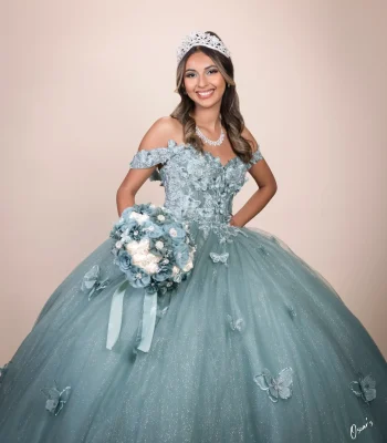 Quinceañera studio portrait in a sage green 3D floral gown with butterfly appliqués, smiling and holding a matching bouquet
