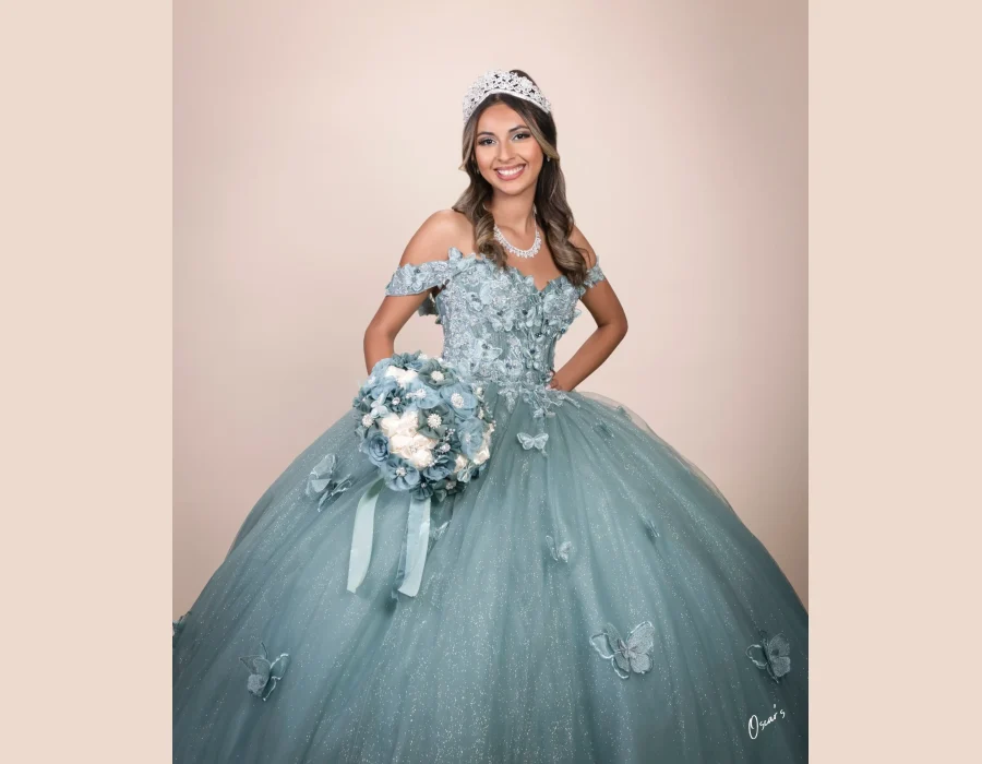 Quinceañera studio portrait in a sage green 3D floral gown with butterfly appliqués, smiling and holding a matching bouquet