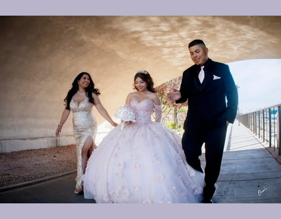 Quinceañera walking portrait in a blush pink floral gown, flanked by family under a tunnel archway