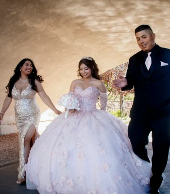 Quinceañera walking portrait in a blush pink floral gown, flanked by family under a tunnel archway