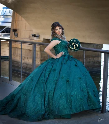 Quinceañera portrait in an emerald green gown, posing on a bridge railing near a marina