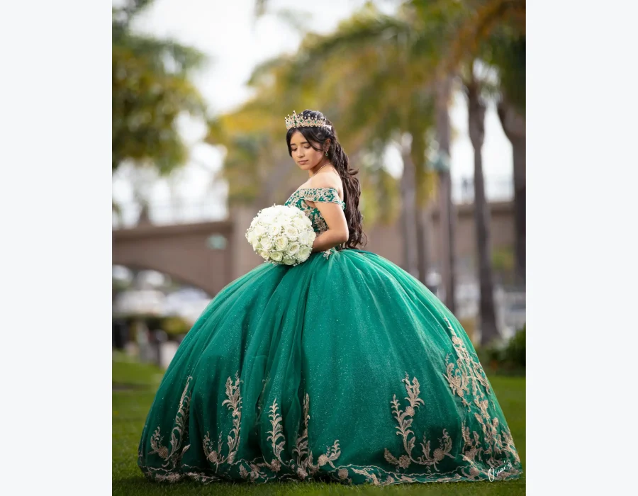 Quinceañera profile portrait in a sage green floral gown, holding a white rose bouquet on a grassy lawn