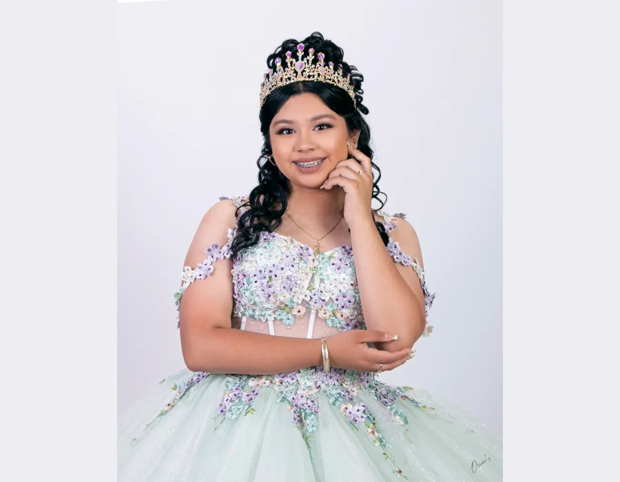 Quinceañera close-up portrait in a champagne beaded gown with a crystal tiara, leaning on a railing near the water
