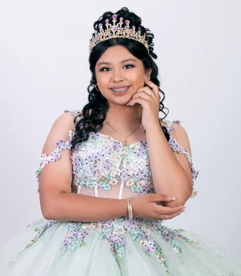 Quinceañera close-up portrait in a champagne beaded gown with a crystal tiara, leaning on a railing near the water