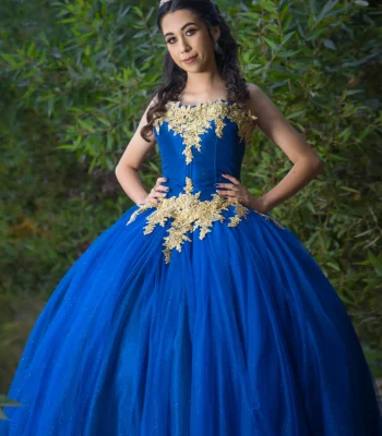 Quinceañera studio portrait in an emerald green gown with gold lace and a matching tiara, holding a green and gold rose bouquet