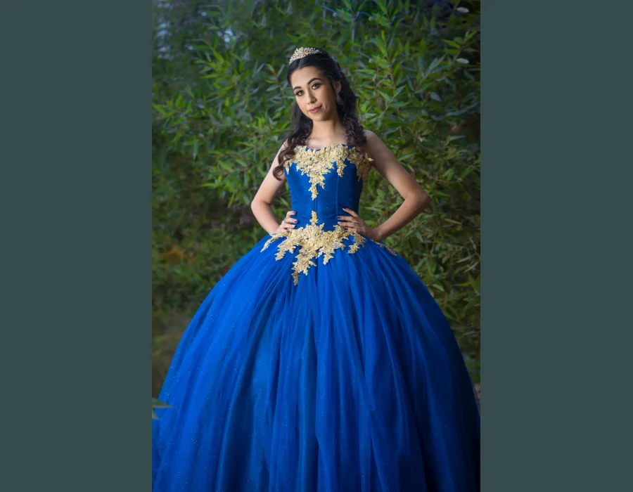 Quinceañera studio portrait in an emerald green gown with gold lace and a matching tiara, holding a green and gold rose bouquet