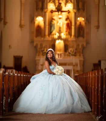 Quinceañera close-up studio portrait in a pastel floral embellished gown with a crystal tiara, smiling with her hand to her cheek