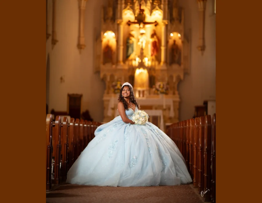 Quinceañera close-up studio portrait in a pastel floral embellished gown with a crystal tiara, smiling with her hand to her cheek