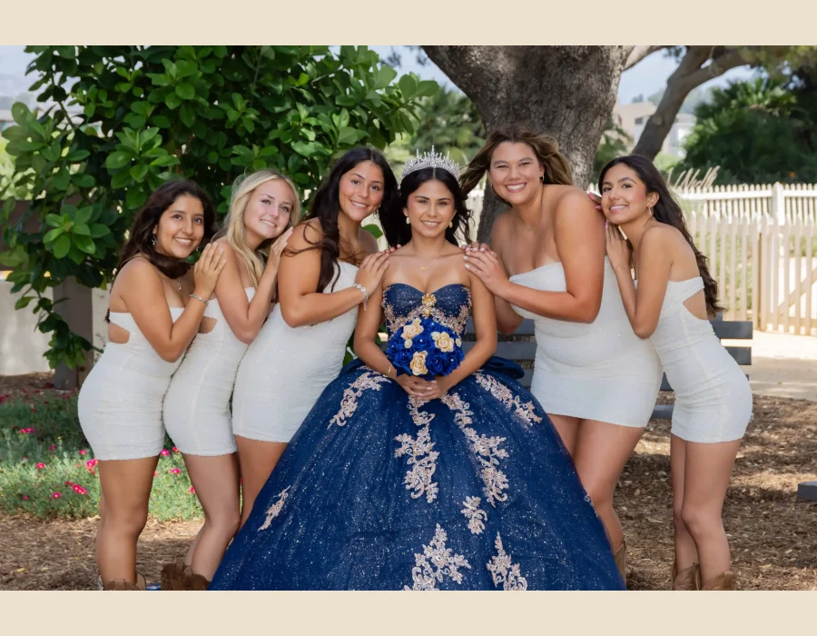 Quinceañera group portrait in a navy blue gown with gold lace, surrounded by friends in matching white dresses
